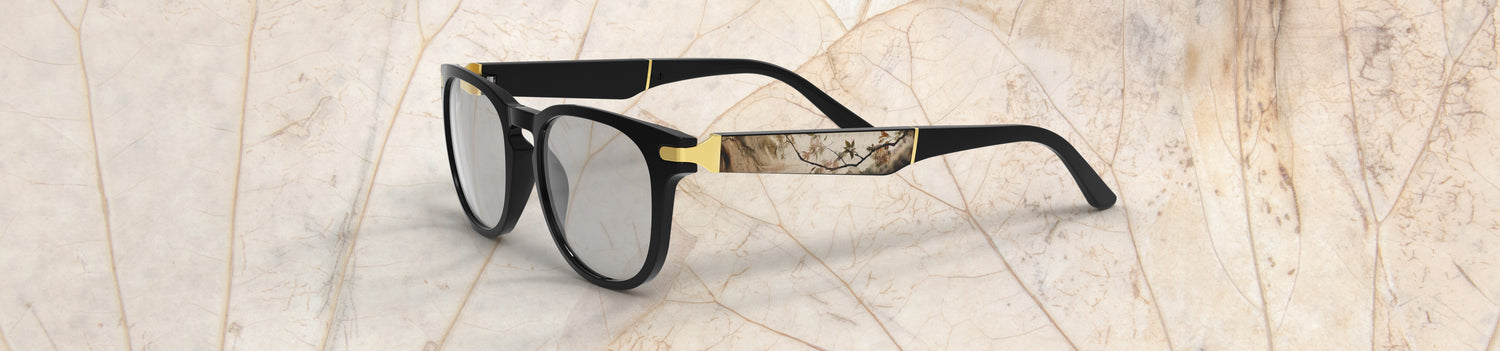 Sunglasses with black frame and gold accents on a light marble background
